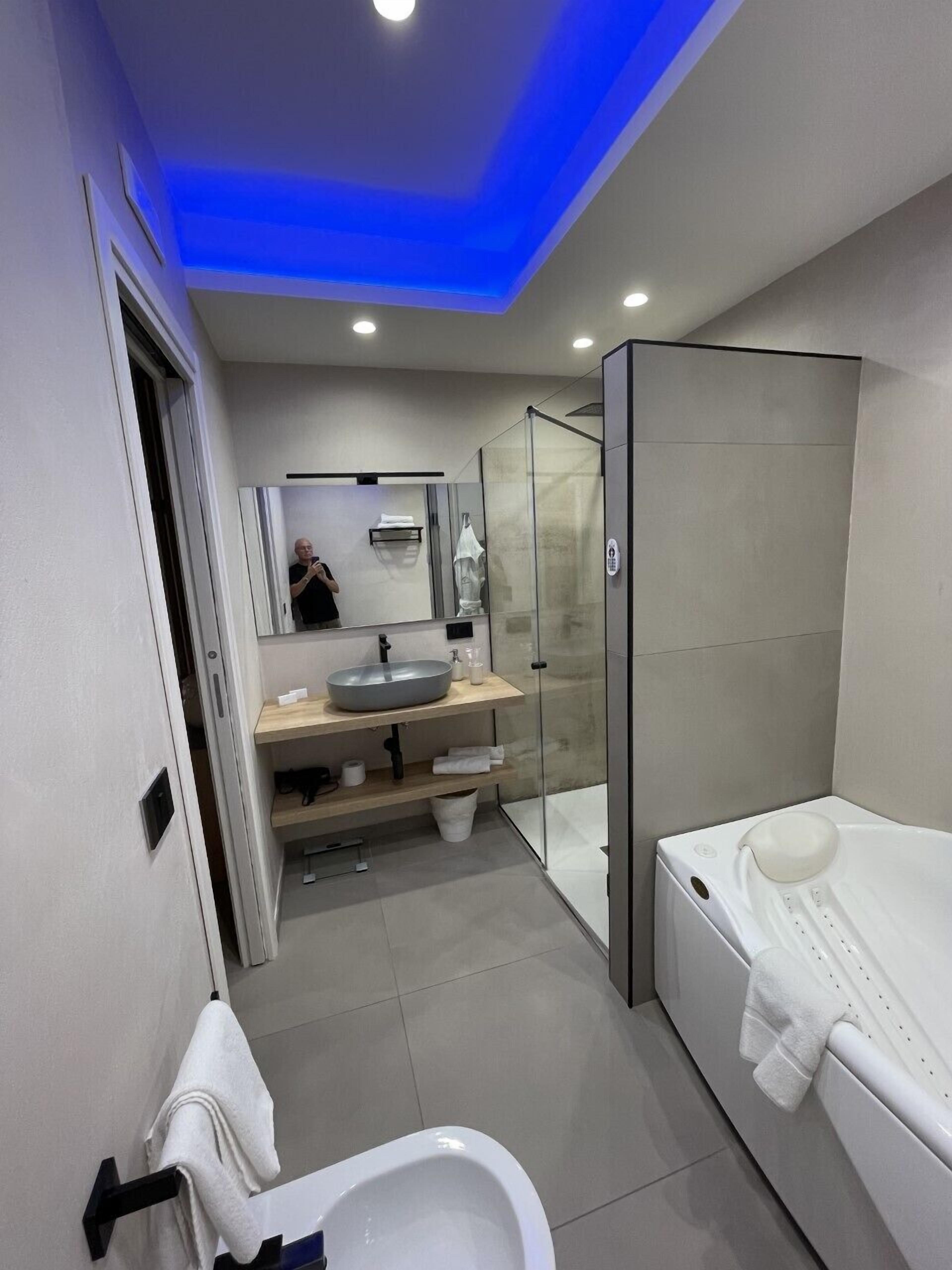 A modern bathroom with a glass shower enclosure, a bathtub, a toilet, and a vanity with a sink and mirror.