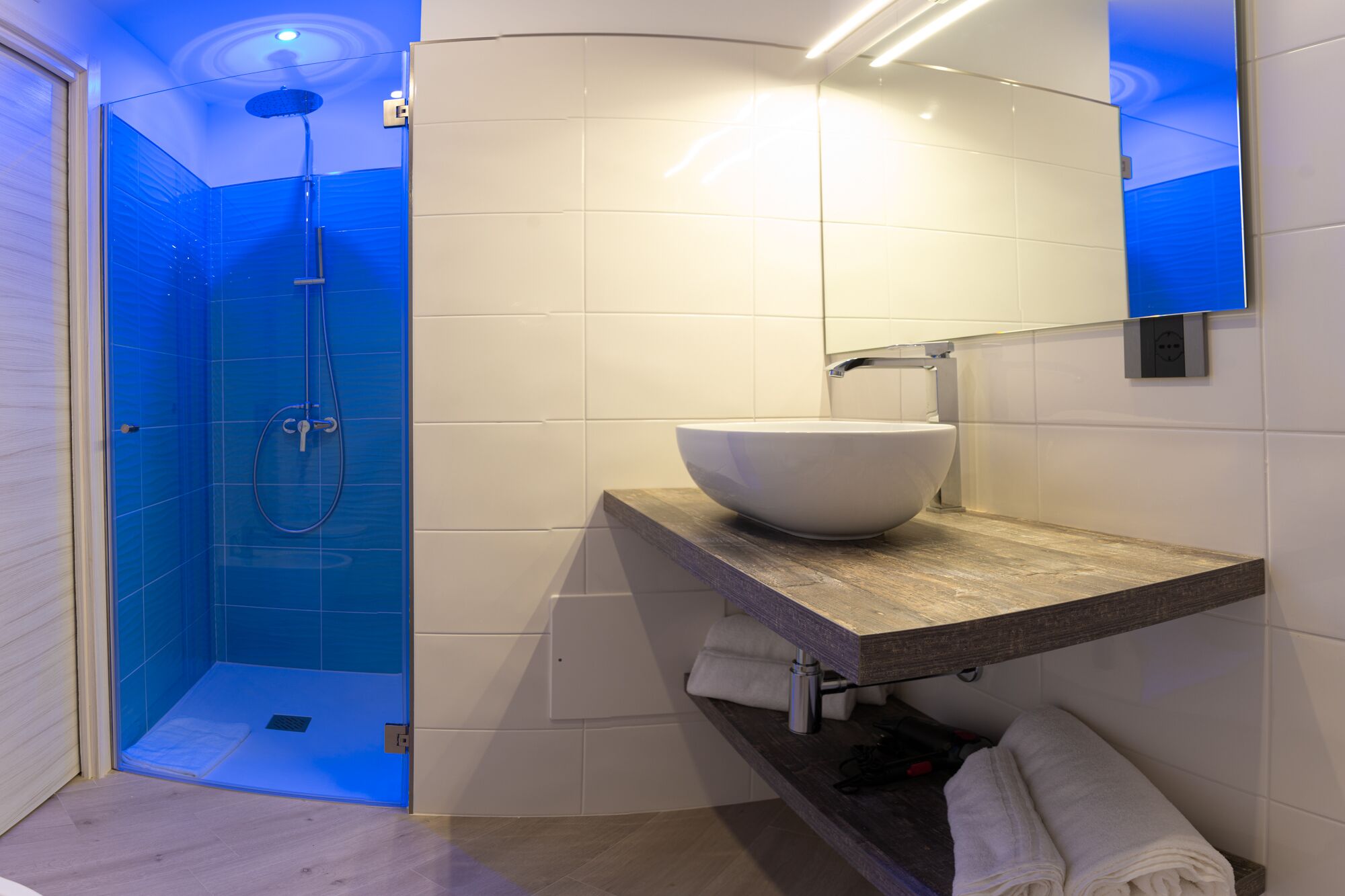 A modern bathroom with a glass-enclosed shower, a white sink on a wooden countertop, and a mirror above the sink.