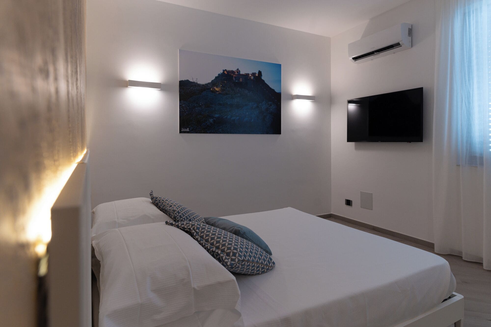 A bedroom with a bed, a mounted TV, and a wall-mounted air conditioner.
