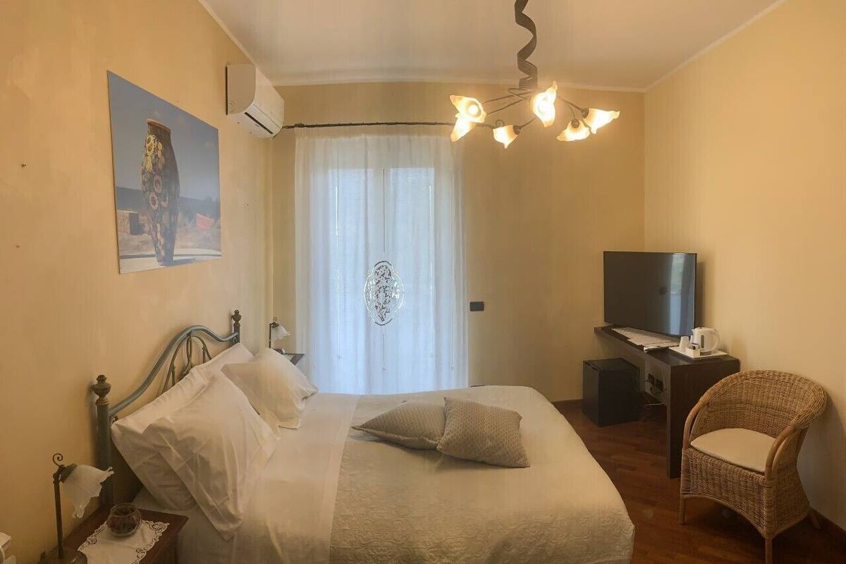 A bedroom with a bed, a chair, a desk, a television, and a window with curtains.