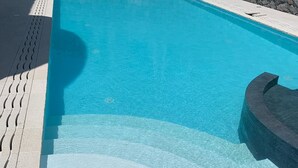Une piscine rectangulaire à l’eau d’un bleu limpide, entourée d’un mur de pierre et d’une terrasse carrelée.