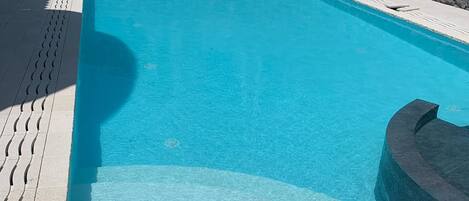 A rectangular swimming pool with clear blue water, surrounded by a stone wall and a tiled deck.
