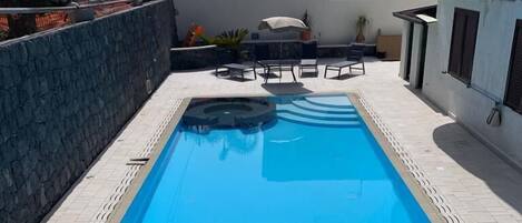 En rektangulär swimmingpool med ett klart, blått vatten och en omgivande poolterrass som är belagd med plattor.