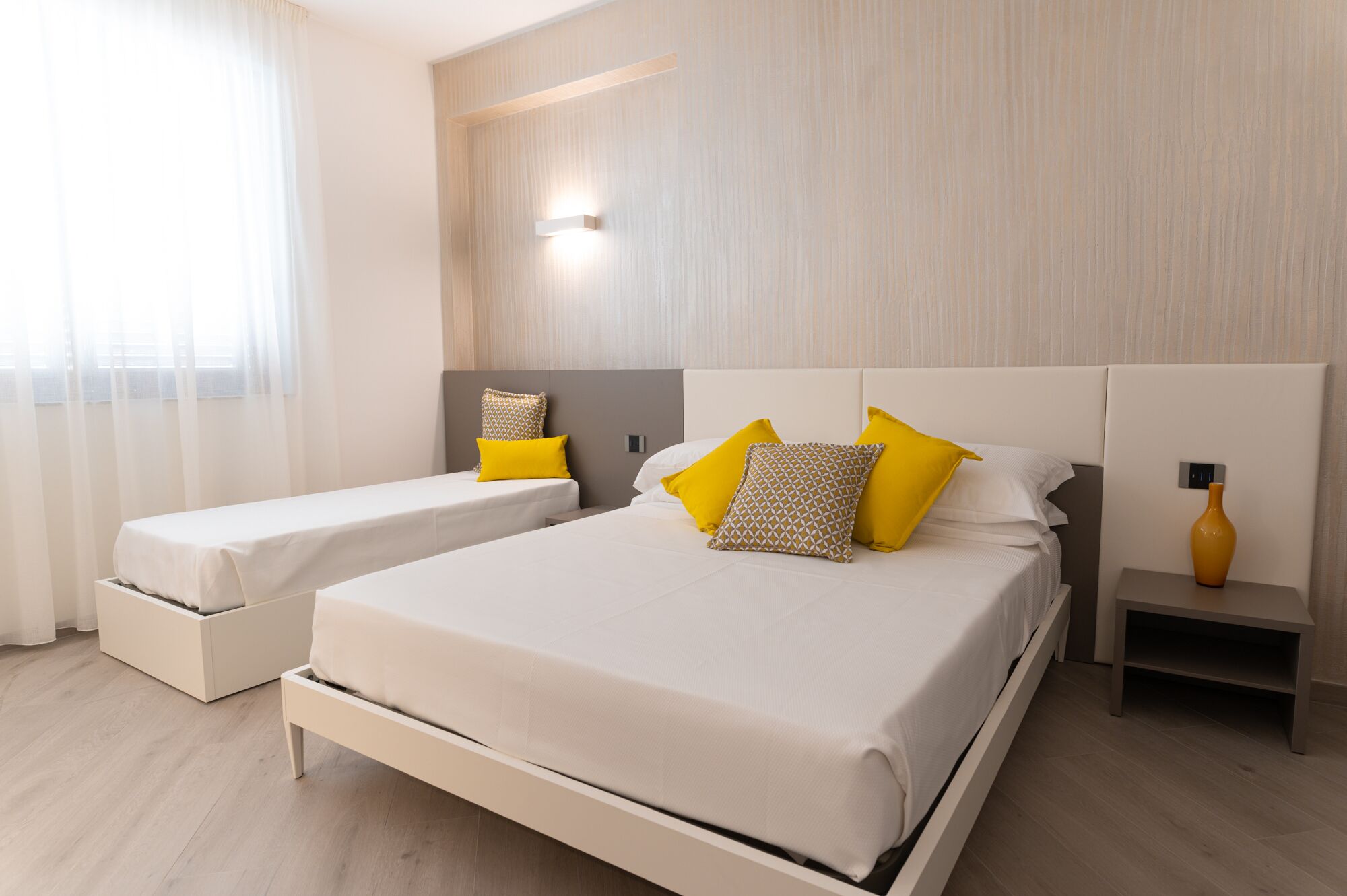 A modern hotel room with a large bed, two bedside tables, and a small table with a vase.