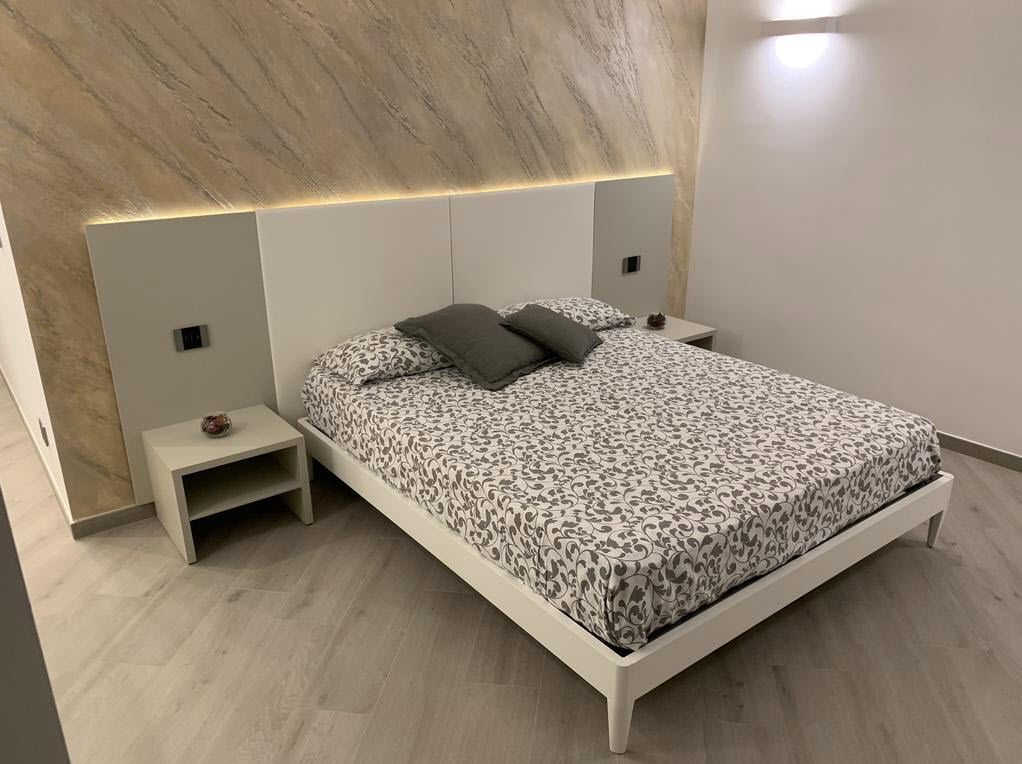 A modern bedroom with a bed, nightstands, and a headboard with integrated lighting.
