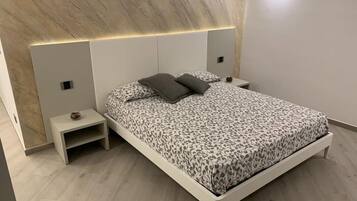 A modern bedroom with a bed, nightstands, and a headboard with integrated lighting.