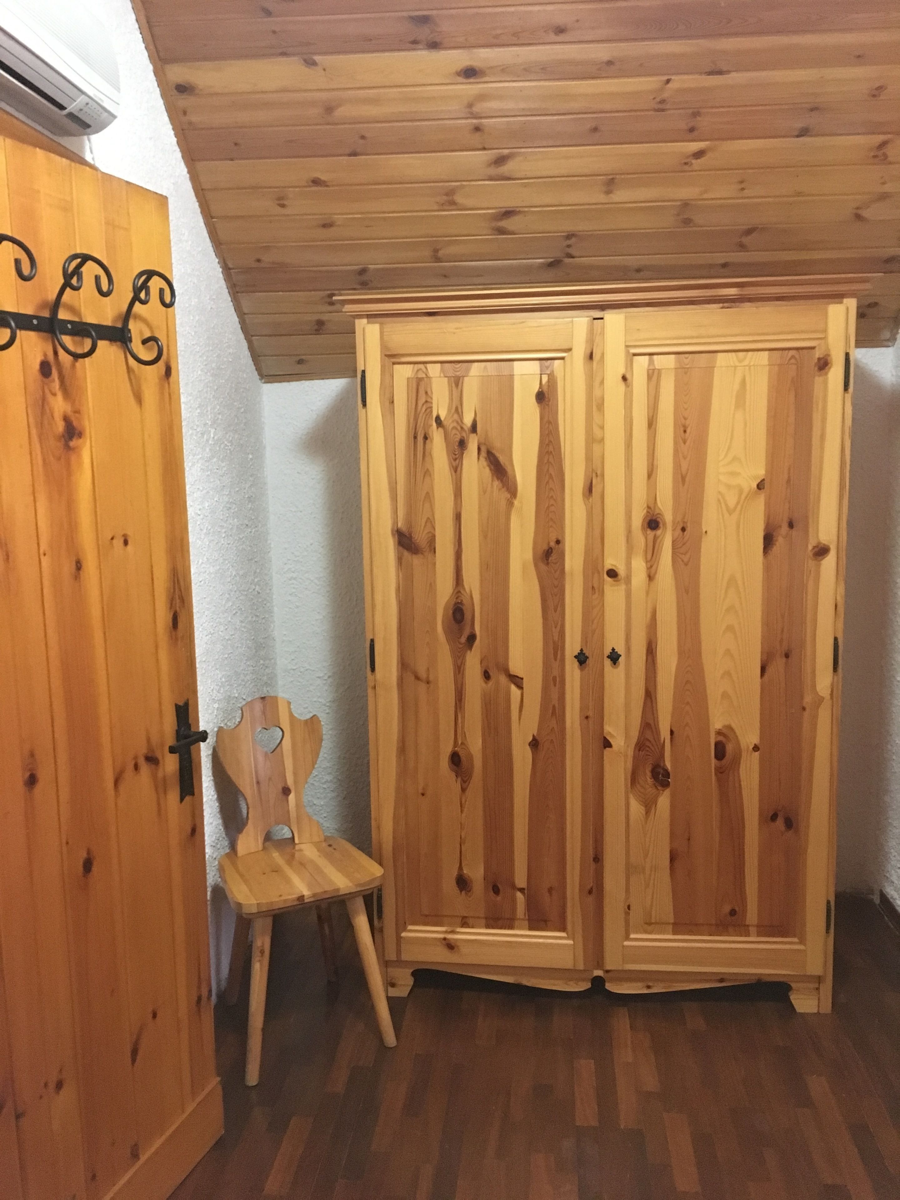Een houten garderobe met twee deuren, een houten stoel en een witte muur.