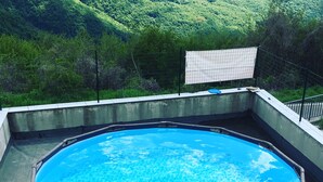 Une piscine octogonale bordée d’osier, entourée d’une terrasse en béton, le tout se fondant dans un paysage de collines verdoyantes.