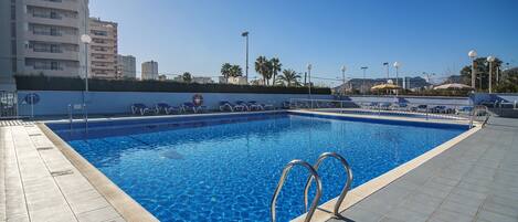 A rectangular swimming pool with clear blue water, surrounded by a tiled deck.