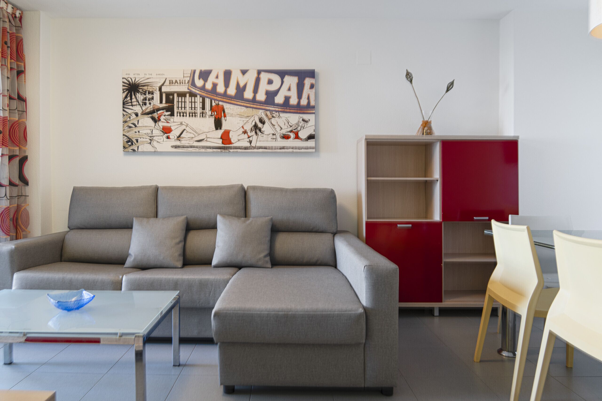 A modern living room with a grey sectional sofa, a small white table, and a red cabinet.