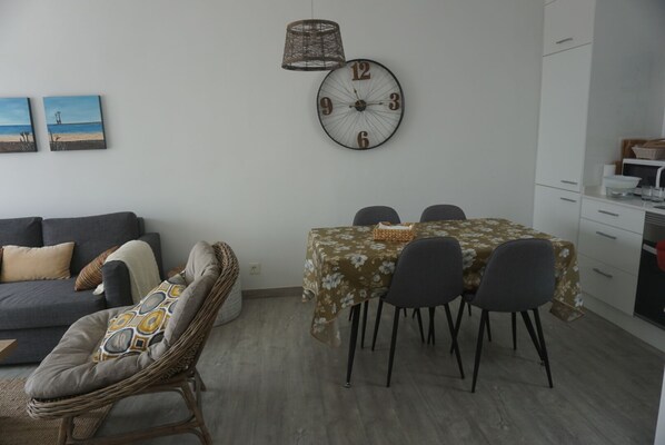 Una sala de estar moderna con un sofá, una mesa de comedor con sillas, una silla de mimbre, un reloj y una pequeña cocina con armarios y un lavabo.