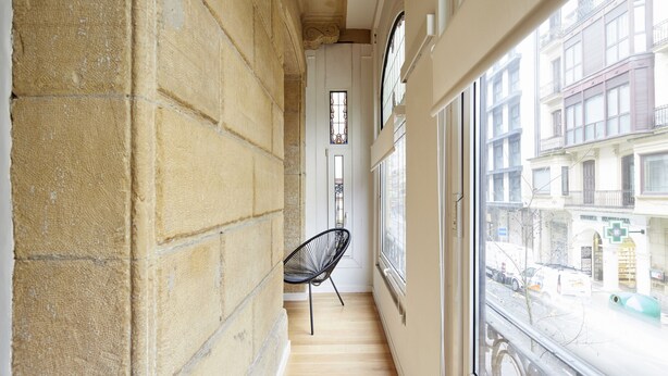 A narrow corridor with a chair, a window, and a door leading to a balcony.