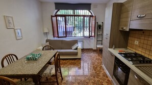 Angolo cottura compatto con zona pranzo, divano e finestra vista verde.