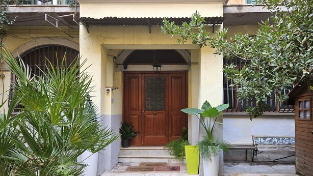 L'ingresso di una casa con una porta di legno, gradini, una panchina e piante in vaso.