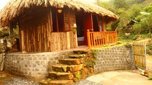 Una casa rústica de madera con techo de paja, un porche de madera y una escalera de piedra que lleva a la entrada.