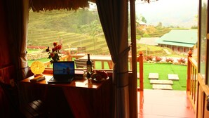 Una habitación con un ordenador portátil sobre una mesa de madera, un jarrón con flores y vistas a campos escalonados al exterior.