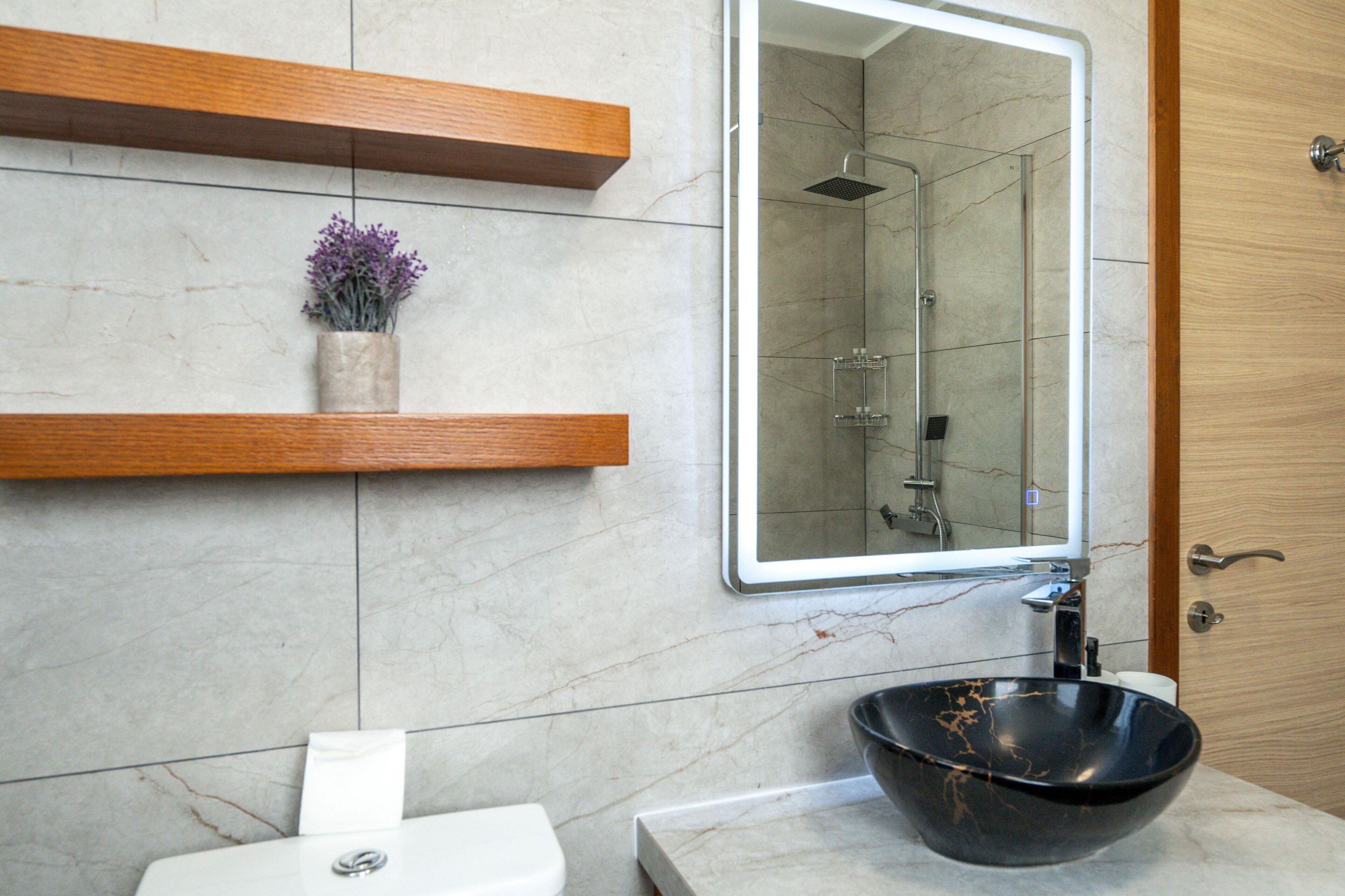 A bathroom with a marble sink, a wooden shelf, a mirror, and a shower.