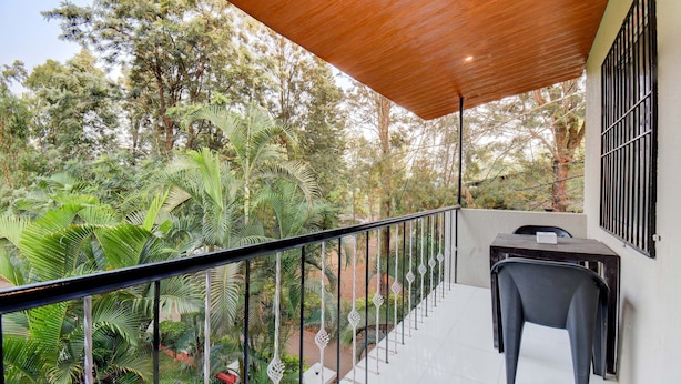 Un balcon doté d’un plafond en bois, une table avec une chaise, et une vue sur une végétation luxuriante.