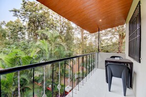 A balcony with a wooden ceiling, a table with a chair, and a view of lush greenery. - Hotel Silver Inn (Mahabaleshwar)