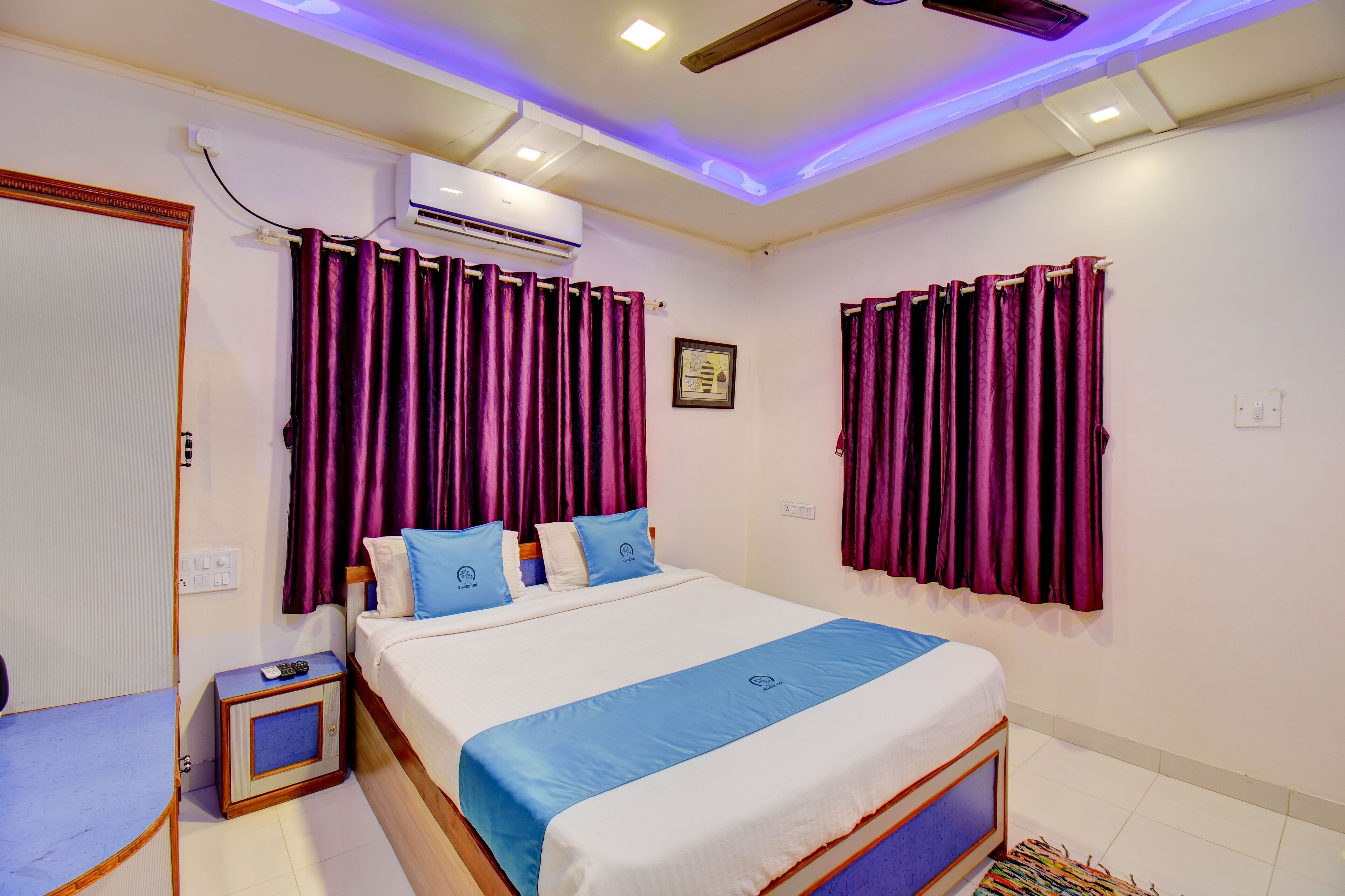 A bedroom with a bed, purple curtains, a ceiling fan, and an air conditioning unit.