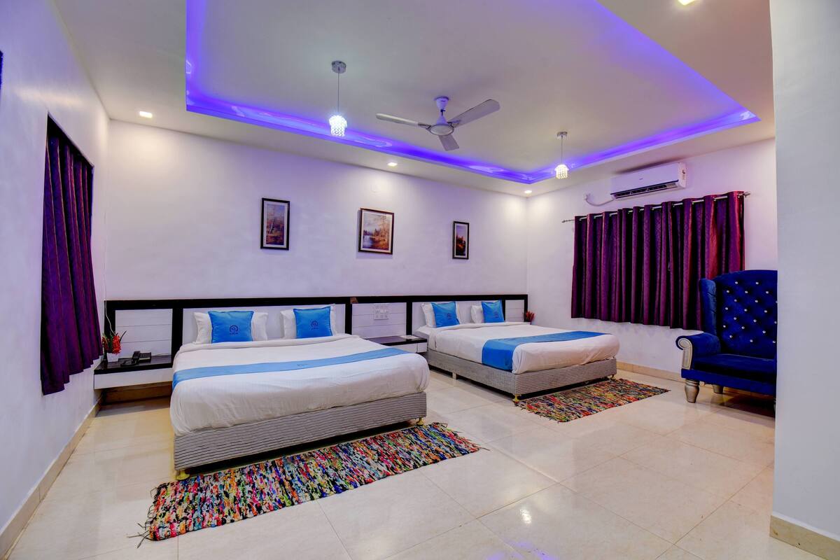 Une chambre d’hôtel moderne avec deux lits, un ventilateur de plafond et un fauteuil bleu.
