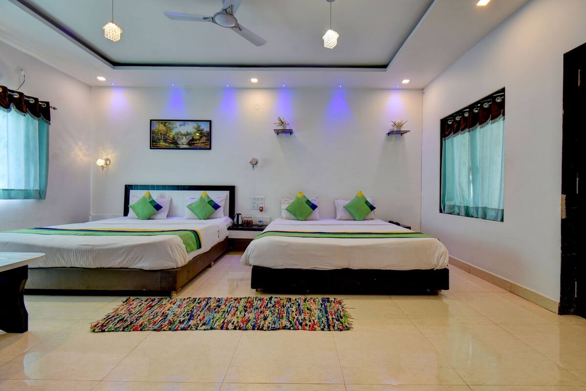 Une chambre d’hôtel avec deux lits, un ventilateur de plafond, des spots encastrés, un tapis coloré et un tableau au mur.