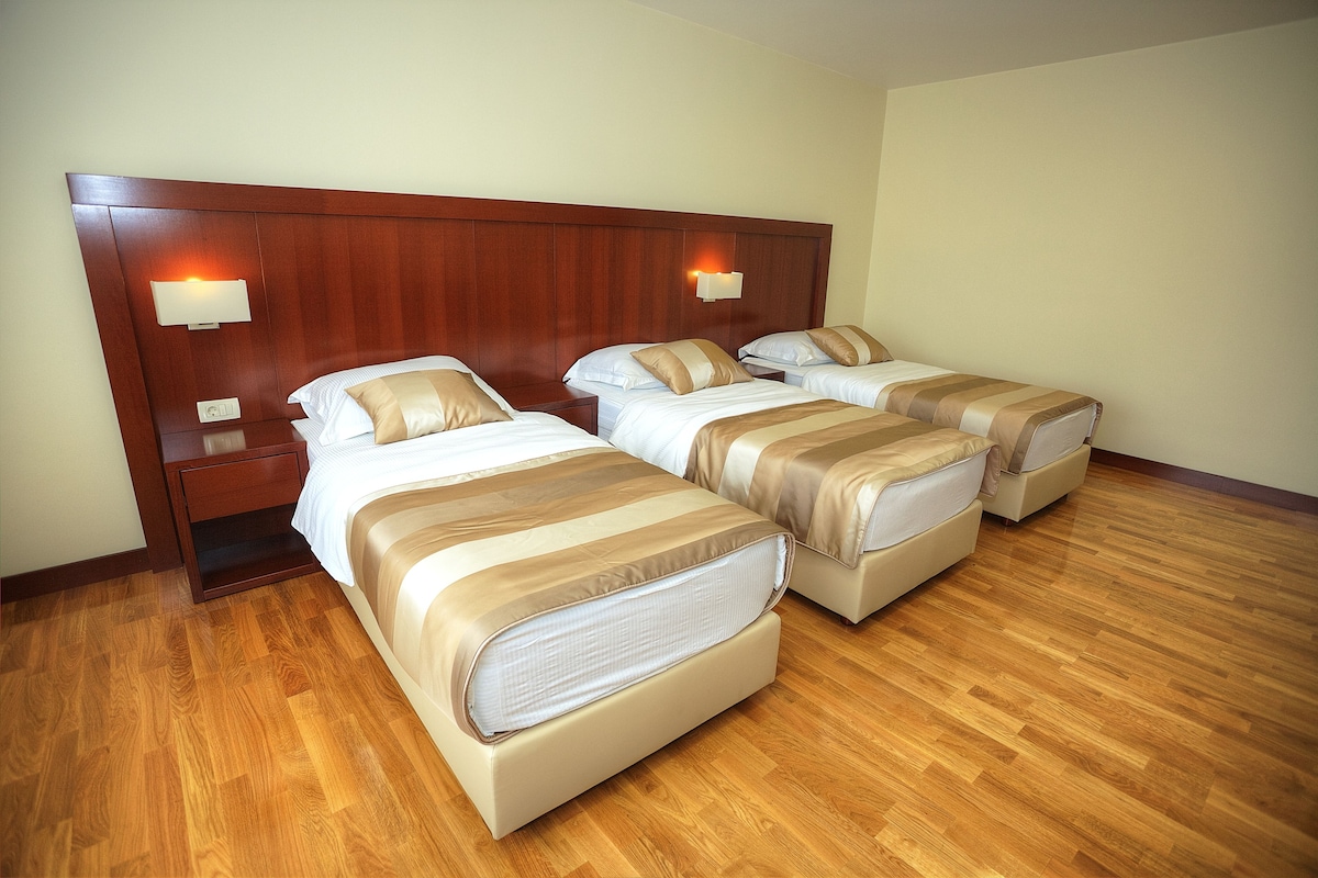 Habitación de hotel con tres camas, suelo de madera y cabecera de madera.