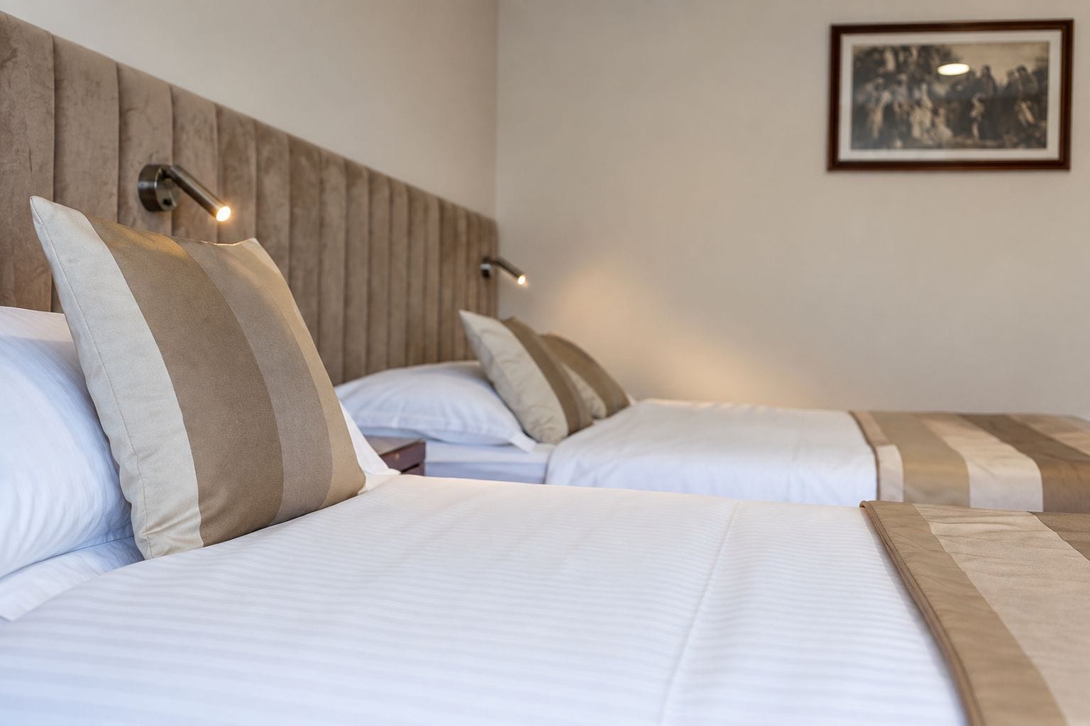 Une chambre d’hôtel avec deux lits, chacun doté d’une tête de lit en bois, de draps blancs et d’un tableau encadré au mur.