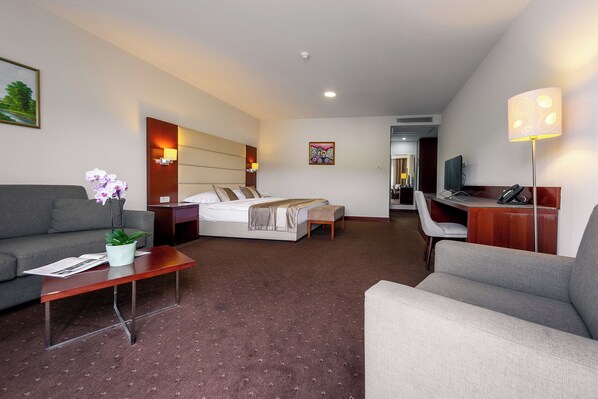 A hotel room with a bed, sofa, desk, and a small table with a plant. - Hotel Palace Medjugorje (Citluk)