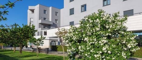 Ein modernes Gebäude mit flacher Fassade, zahlreichen Fenstern und einem gepflegten Rasen mit einem blühenden Baum.