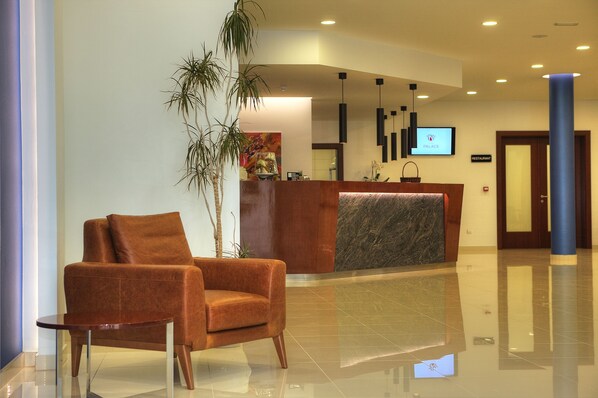 Un moderno vestíbulo de hotel con mostrador de recepción, un sillón cómodo y una planta grande.