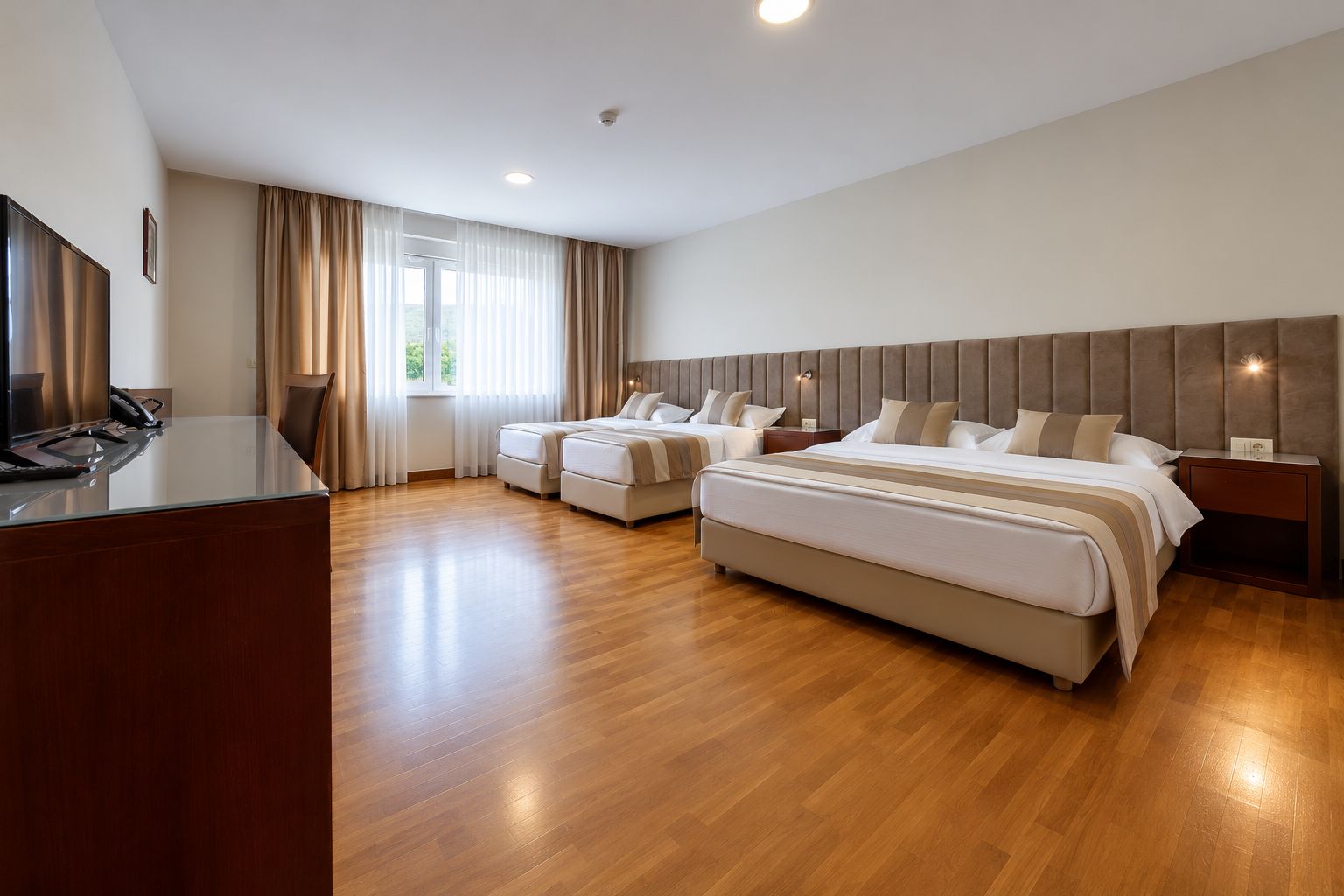 Une chambre d’hôtel avec un grand lit, un lit plus petit, un bureau avec un téléphone et une fenêtre avec des rideaux.