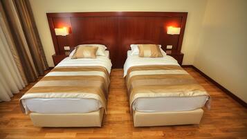 A hotel room with two beds, wooden headboard, bedside lamps, and a wooden floor.