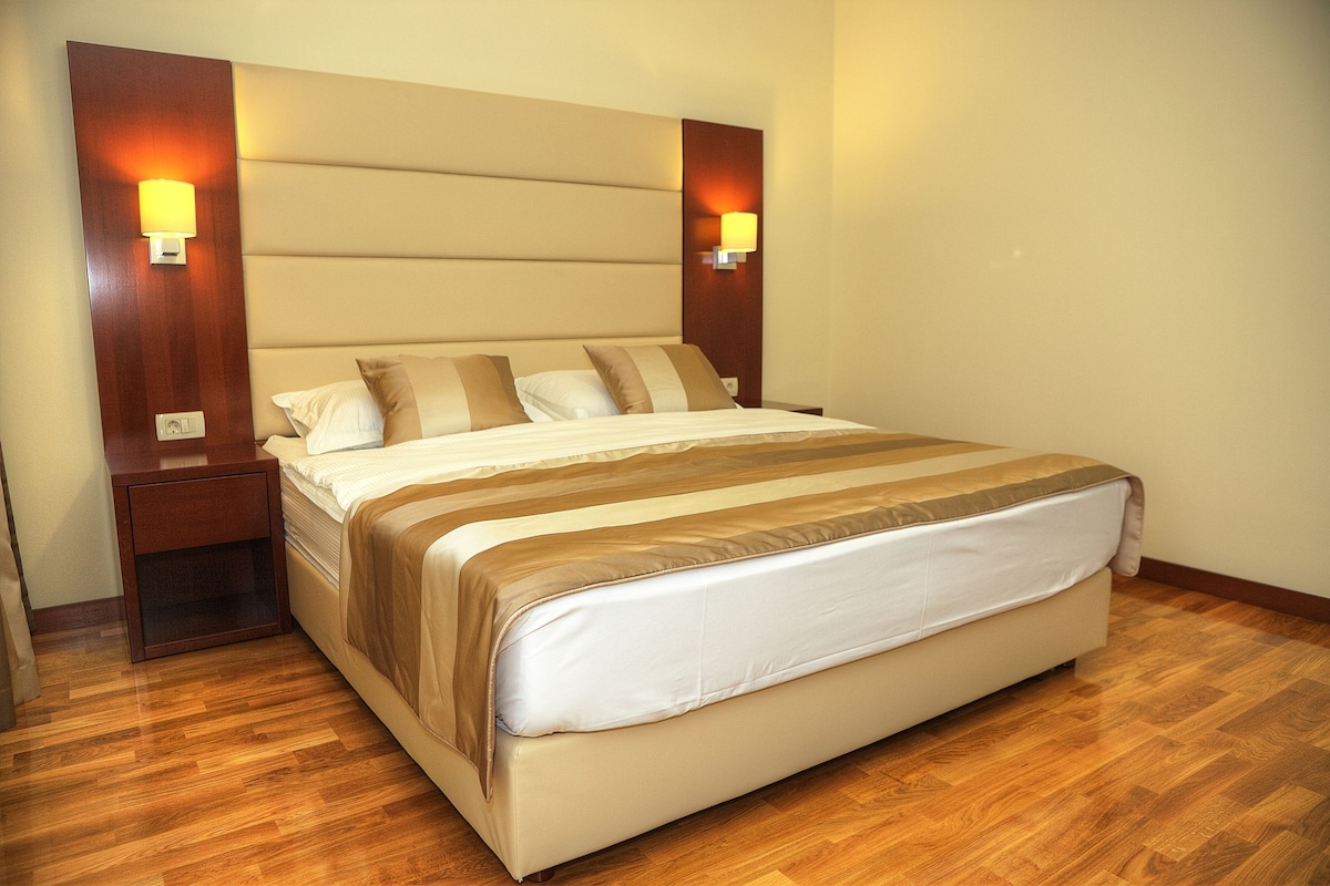 Una cama bien hecha con cabecera, dos mesitas de noche y lámparas fijadas a la pared.