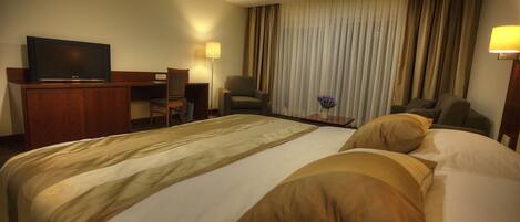 A hotel room with a large bed, two armchairs, a desk with a television, and a lamp.