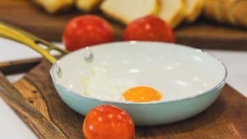 Desayuno con huevos, tomates y pan sobre una tabla de madera.