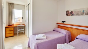 Quarto de hotel com duas camas, uma escrivaninha e uma janela com cortinas.