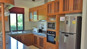 A kitchen with wooden cabinets, stainless steel appliances, a granite countertop, and a window with a view of greenery. - 4 Bedroom Villa with Private Pool in Walled Garden (Mae Nam)