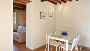 A dining area with a white table and chairs, a blue bowl on the table, and two framed pictures on the wall. - Lovely cottage in the park of a Renaissance Villa (Capannori)