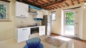 A compact kitchen with white cabinets, a gas stove, and a refrigerator. There is a dining table with a blue bowl and a map. - Lovely cottage in the park of a Renaissance Villa (Capannori)