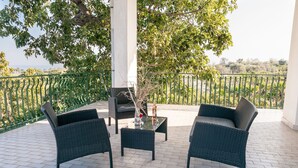 Eine Terrasse mit Korbmöbeln, einem Glastisch und einer Vase mit getrockneten Ästen.