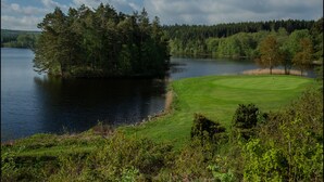 Un parcours de golf avec un plan d’eau et une zone boisée.
