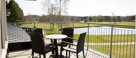 Una terraza techada al aire libre con una mesa y sillas, con vista a un área verde y un cuerpo de agua.