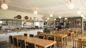 Un restaurant avec des tables et des chaises en bois, un comptoir avec une caisse enregistreuse et des luminaires suspendus.