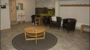 A room with a round wooden table, four black leather chairs, a small round table with two wine glasses, a shower area, a sink, and a wall-mounted towel rack.