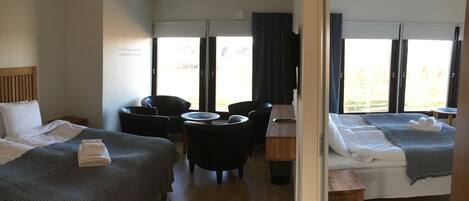 Una habitación de hotel con dos camas, una mesita, dos sillas y una ventana con cortinas.
