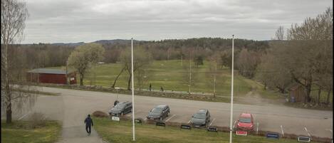A parking lot with several cars, a person walking, and a red barn in the background.