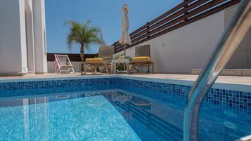 Una piscina azul cristalina con sillas de descanso y una palmera.
