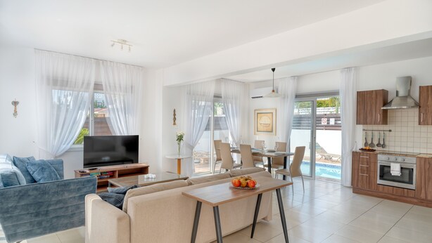 A modern living room with a sofa, TV, and dining area. - Narcissos Villa 2 (Paralimni)