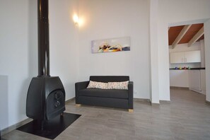 Una sala moderna con un sofá negro, una chimenea y una cocina al fondo.
